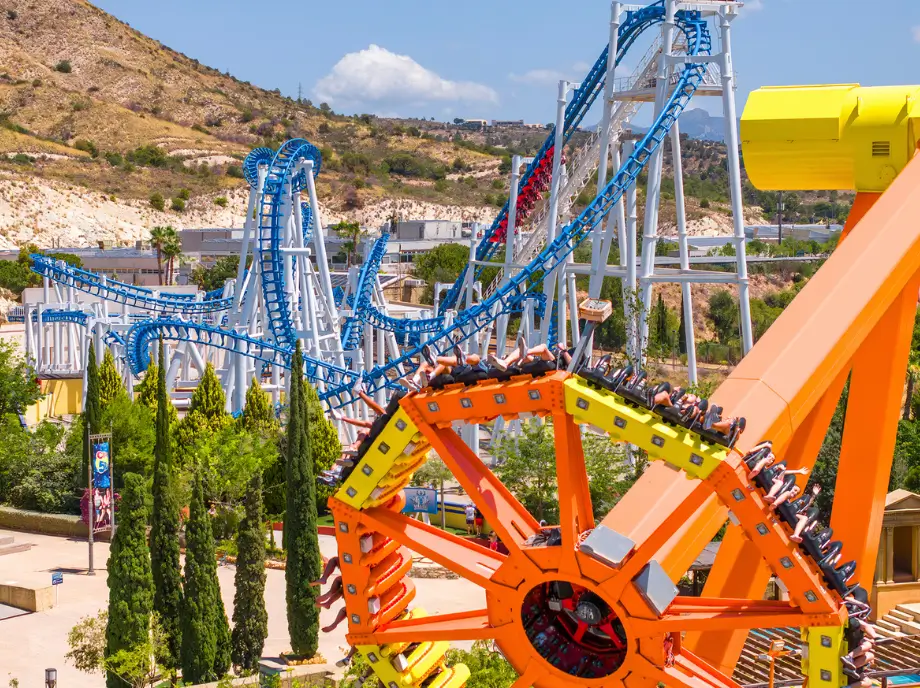 Atracciones mecánicas y montaña rusa en Terra Mítica Benidorm rodeadas de vegetación.