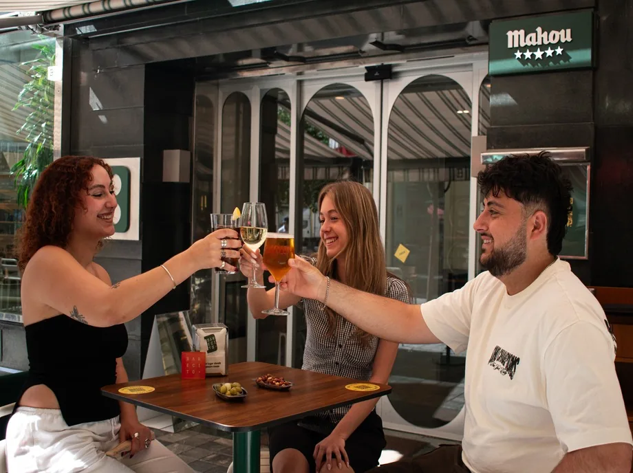 Tres amigos brindando con cerveza y vino en la terraza de Barecito en Valencia