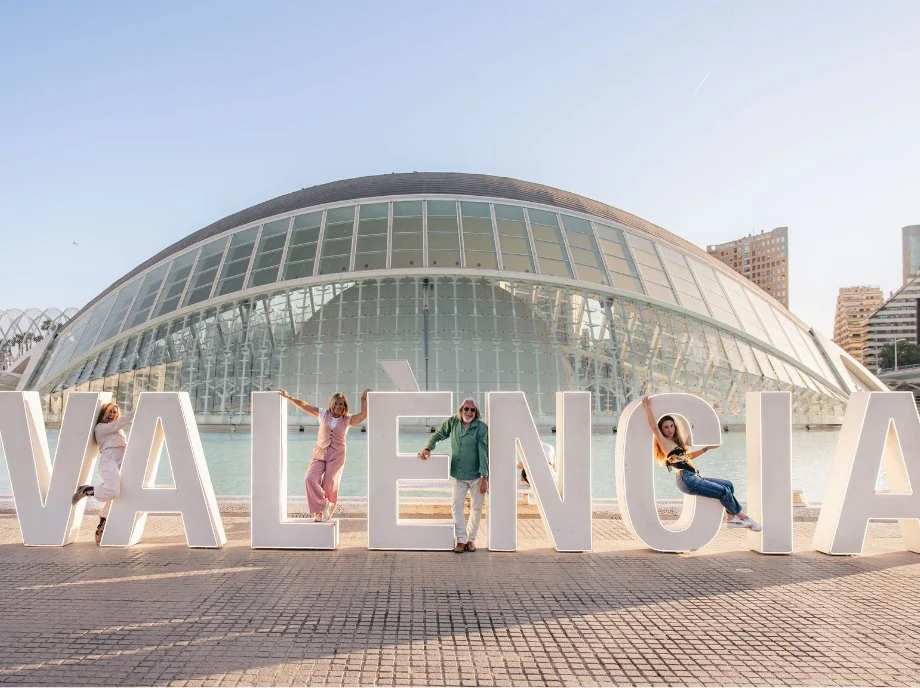 Famiglia che salta accanto all'insegna gigante di Valencia davanti all'Hemisfèric, nella Città delle Arti e delle Scienze.