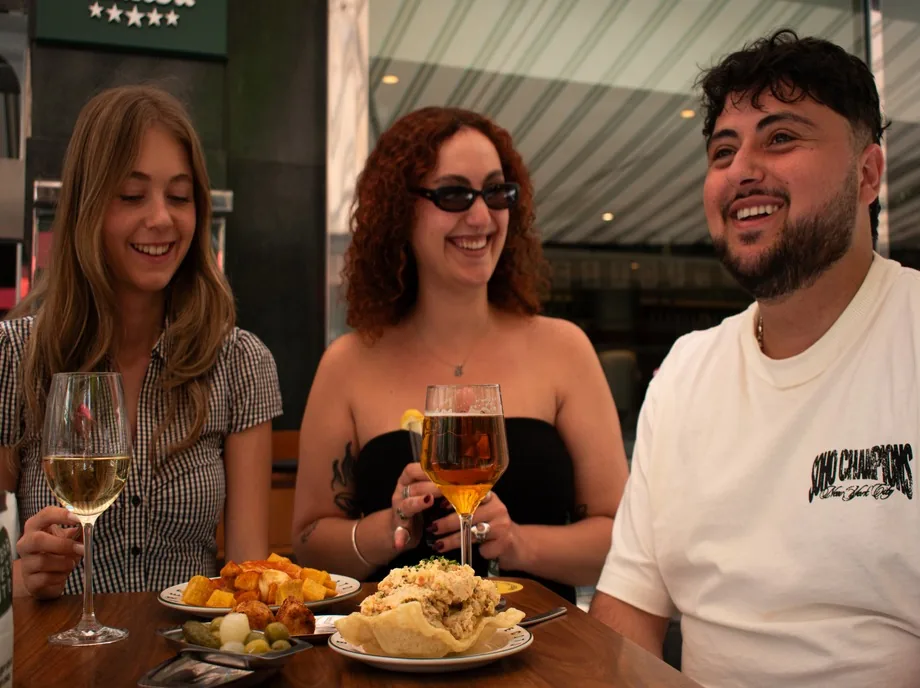 Tres amigos brindando con vino y cerveza junto a patatas bravas y ensaladilla rusa en Valencia
