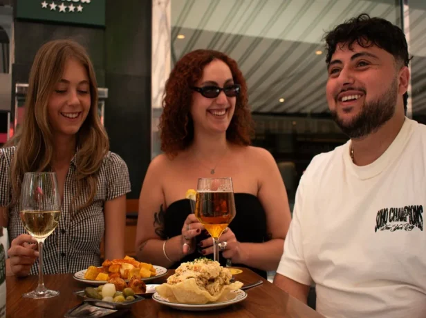 Trois amis trinquent avec du vin et de la bière autour de patatas bravas et d'ensaladilla rusa à Valence.