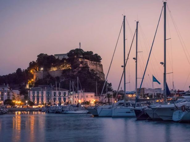 Castillo de Dénia iluminado al atardecer sobre el puerto deportivo
